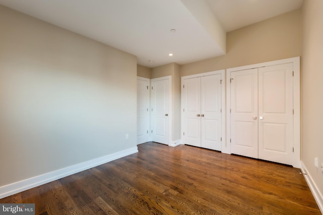 unfurnished bedroom with two closets and dark hardwood / wood-style floors