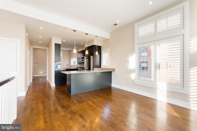 kitchen with kitchen peninsula, stainless steel fridge, dark hardwood / wood-style flooring, hanging light fixtures, and a breakfast bar area