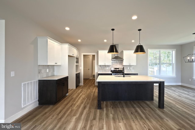 kitchen with decorative backsplash, a kitchen island with sink, stainless steel range oven, white cabinets, and hardwood / wood-style floors