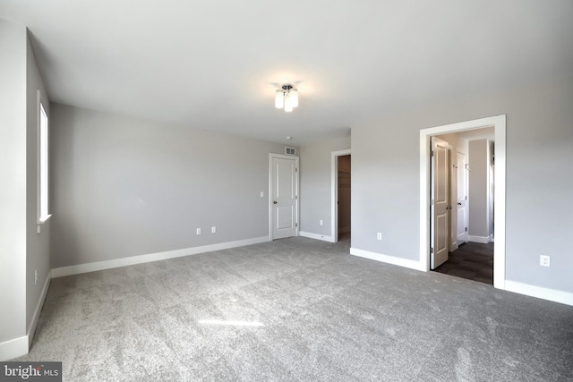 unfurnished bedroom featuring dark colored carpet, connected bathroom, a spacious closet, and a closet