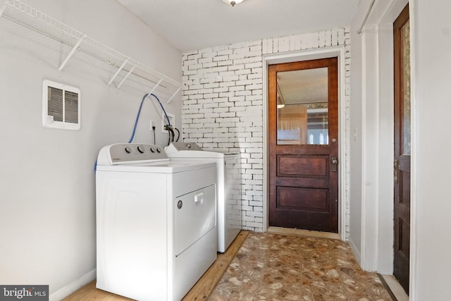 clothes washing area with washing machine and dryer and brick wall