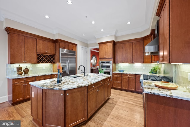 kitchen with an island with sink, light wood-type flooring, range hood, and appliances with stainless steel finishes