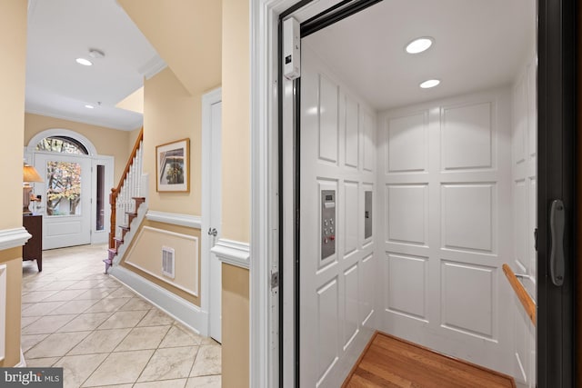 hallway with elevator, light tile patterned floors, and ornamental molding