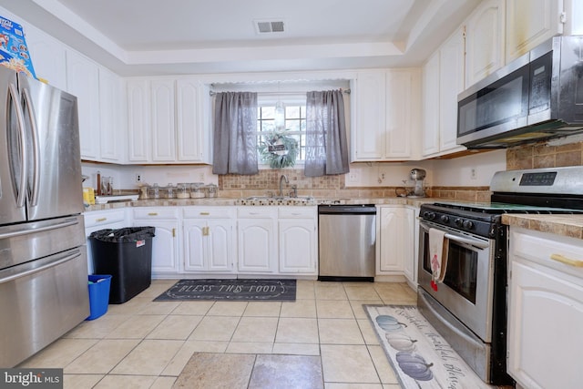 kitchen featuring sink, stainless steel appliances, a raised ceiling, white cabinets, and light tile patterned flooring