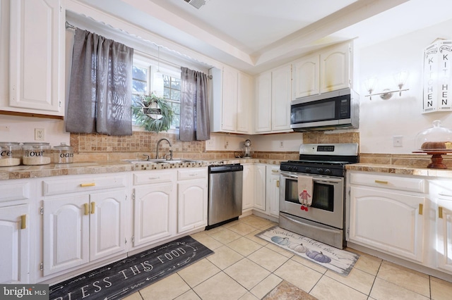 kitchen with stainless steel appliances, a sink, light tile patterned floors, white cabinets, and decorative backsplash