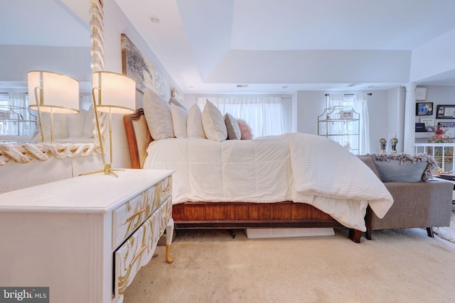 bedroom with a raised ceiling, ornate columns, and light colored carpet