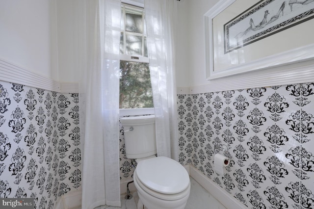 half bath with toilet, a wainscoted wall, and tile walls