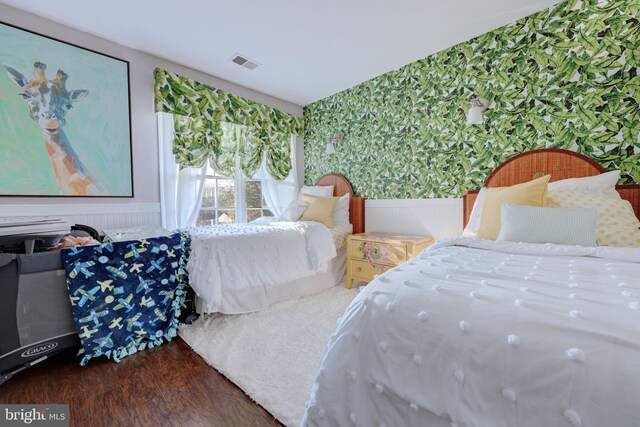 bedroom with wallpapered walls, wainscoting, and wood finished floors
