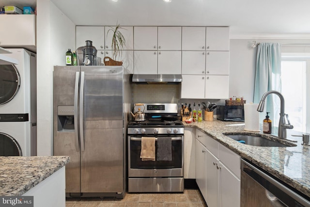 kitchen featuring light stone countertops, appliances with stainless steel finishes, sink, white cabinets, and stacked washer / drying machine