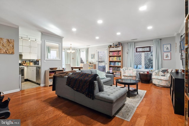 living room with crown molding, an inviting chandelier, and light wood-type flooring