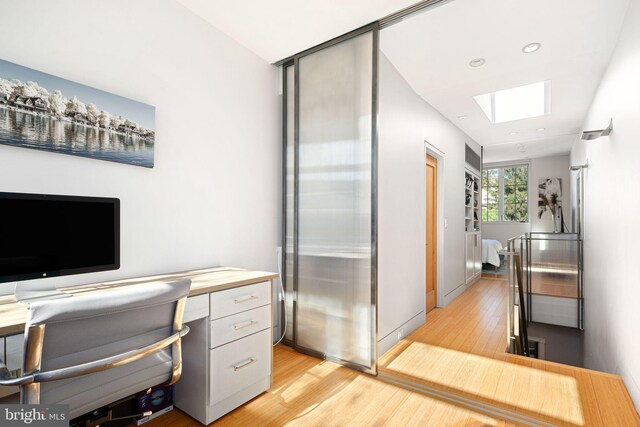 office space with built in desk, light wood-type flooring, and a skylight