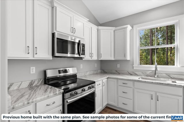 kitchen with light stone countertops, white cabinetry, sink, stainless steel appliances, and lofted ceiling