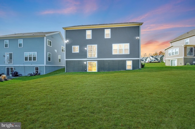 back house at dusk featuring a lawn