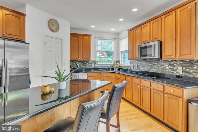 kitchen with backsplash, dark stone counters, sink, light wood-type flooring, and stainless steel appliances