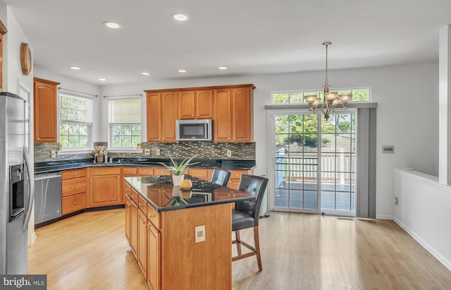 kitchen featuring a kitchen breakfast bar, stainless steel appliances, pendant lighting, light hardwood / wood-style flooring, and a kitchen island