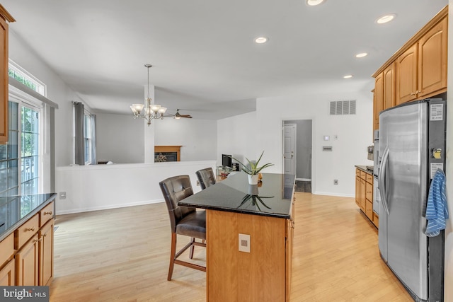 kitchen with light wood-type flooring, a breakfast bar, pendant lighting, stainless steel fridge with ice dispenser, and a kitchen island