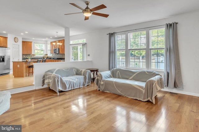 living room with ceiling fan with notable chandelier and light wood-type flooring