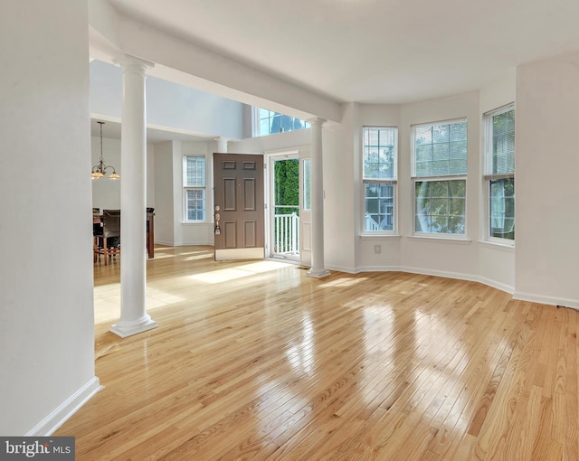 spare room with a notable chandelier, light hardwood / wood-style floors, and ornate columns