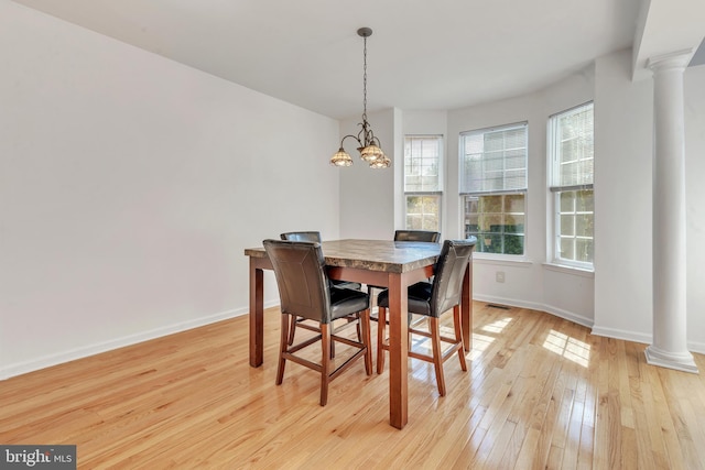 dining area featuring light hardwood / wood-style floors, ornate columns, and a chandelier