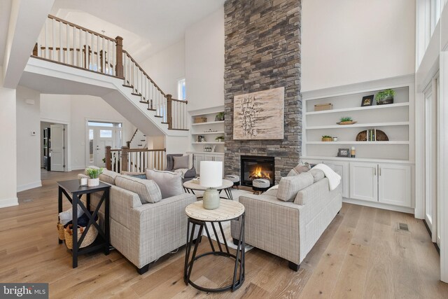 living room with light hardwood / wood-style floors, a stone fireplace, and a towering ceiling