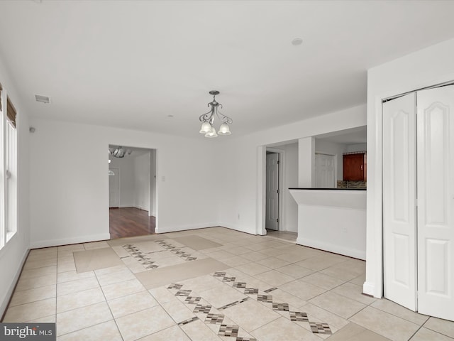 tiled spare room featuring an inviting chandelier