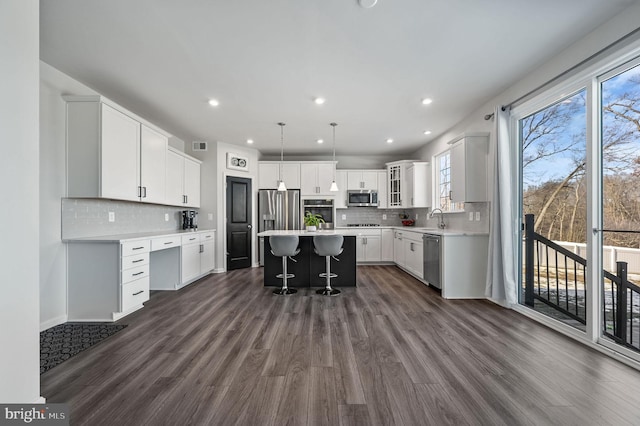 kitchen featuring white cabinetry, a kitchen bar, hanging light fixtures, a center island, and stainless steel appliances