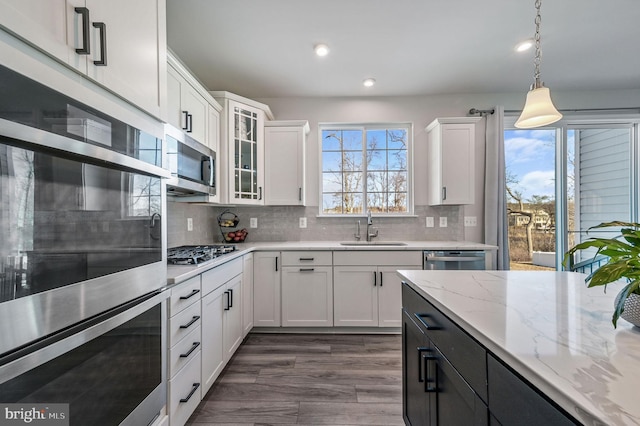 kitchen featuring appliances with stainless steel finishes, a wealth of natural light, sink, white cabinets, and hanging light fixtures