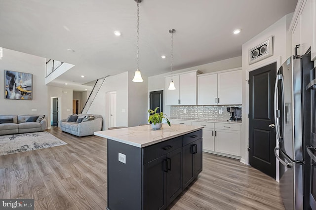 kitchen with white cabinetry, hanging light fixtures, stainless steel fridge, and an island with sink