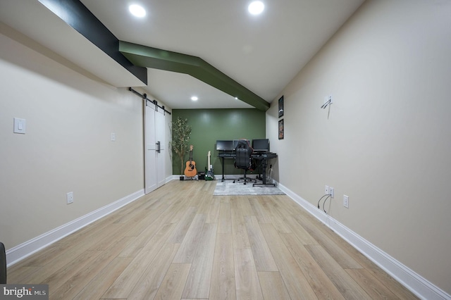 unfurnished office with vaulted ceiling, a barn door, and light hardwood / wood-style flooring