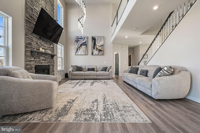 living room featuring a stone fireplace, wood-type flooring, and a high ceiling