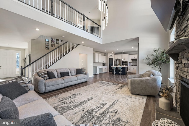 living room featuring a high ceiling, a stone fireplace, and dark hardwood / wood-style flooring