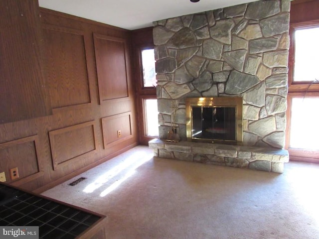 unfurnished living room with carpet, a stone fireplace, and plenty of natural light