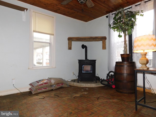 living room featuring wood ceiling, a wood stove, a wealth of natural light, and ceiling fan