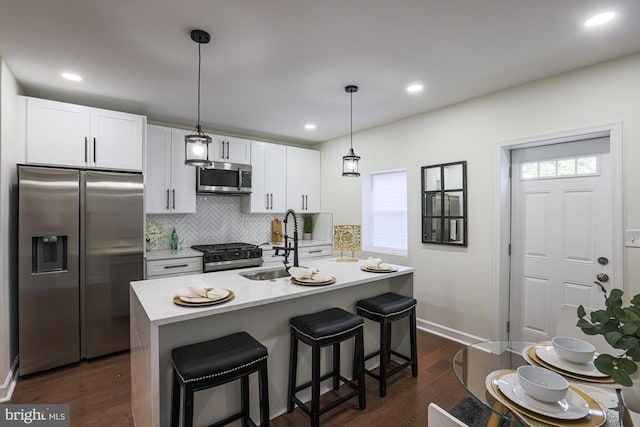 kitchen with white cabinetry, hanging light fixtures, stainless steel appliances, dark wood-type flooring, and a center island with sink