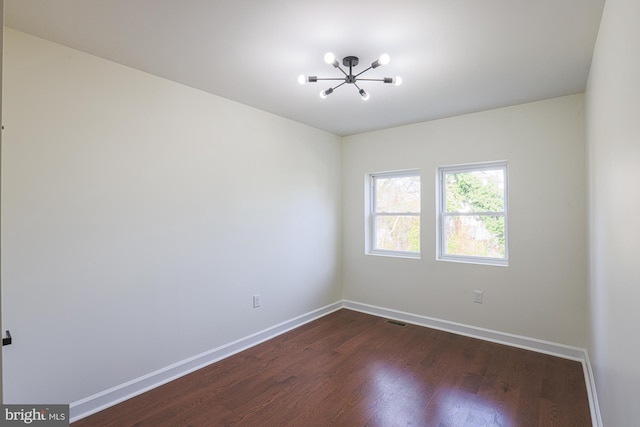 spare room with dark hardwood / wood-style floors and a chandelier