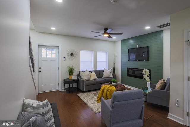 living room featuring ceiling fan, a large fireplace, a healthy amount of sunlight, and dark hardwood / wood-style floors