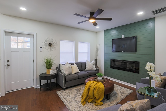 living room featuring ceiling fan, a large fireplace, a wealth of natural light, and dark hardwood / wood-style floors