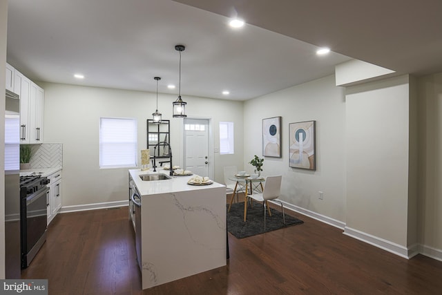 kitchen with sink, white cabinetry, hanging light fixtures, stainless steel appliances, and an island with sink