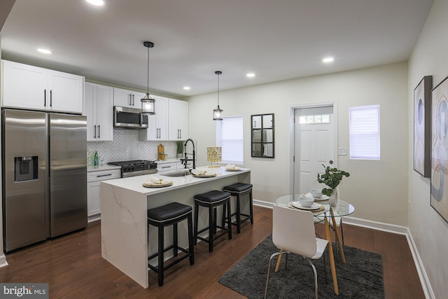 kitchen with appliances with stainless steel finishes, decorative light fixtures, an island with sink, sink, and white cabinets