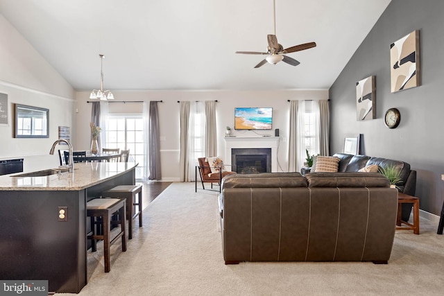 carpeted living room with ceiling fan with notable chandelier, high vaulted ceiling, and sink