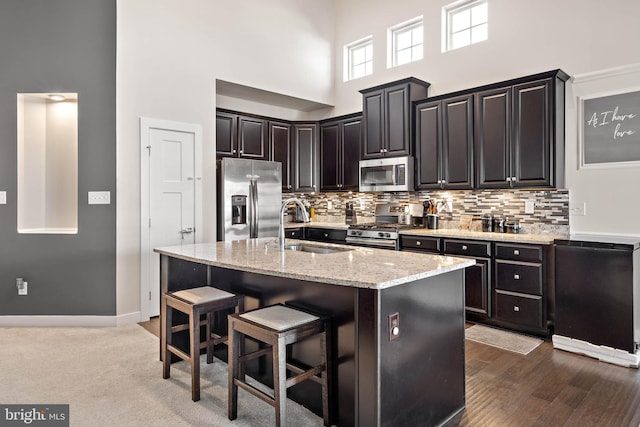 kitchen with sink, a kitchen breakfast bar, a towering ceiling, an island with sink, and appliances with stainless steel finishes