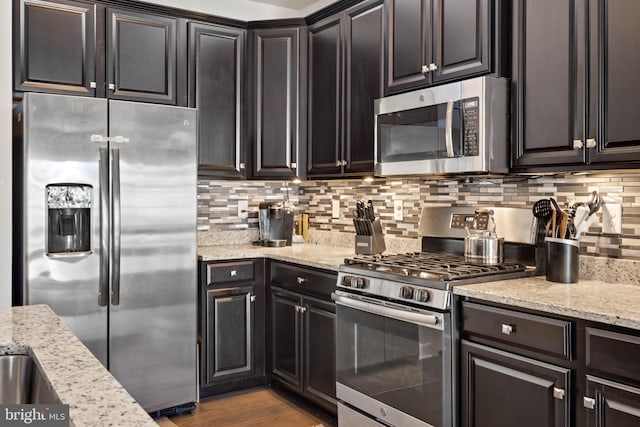 kitchen with light stone countertops, backsplash, dark brown cabinetry, stainless steel appliances, and light hardwood / wood-style flooring