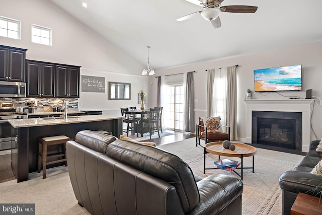 living room with ceiling fan with notable chandelier, light colored carpet, high vaulted ceiling, and sink