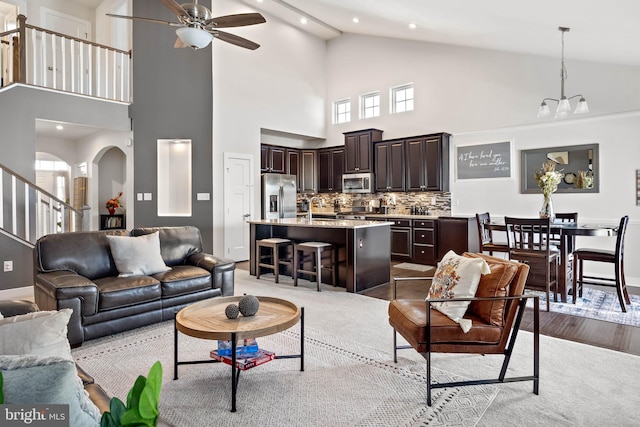 living room with ceiling fan with notable chandelier, light hardwood / wood-style floors, and high vaulted ceiling