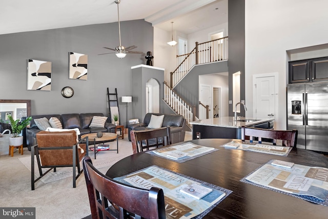 carpeted dining area with ceiling fan, sink, and high vaulted ceiling