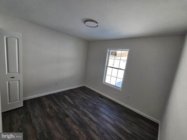 empty room with dark wood-style floors, visible vents, and baseboards