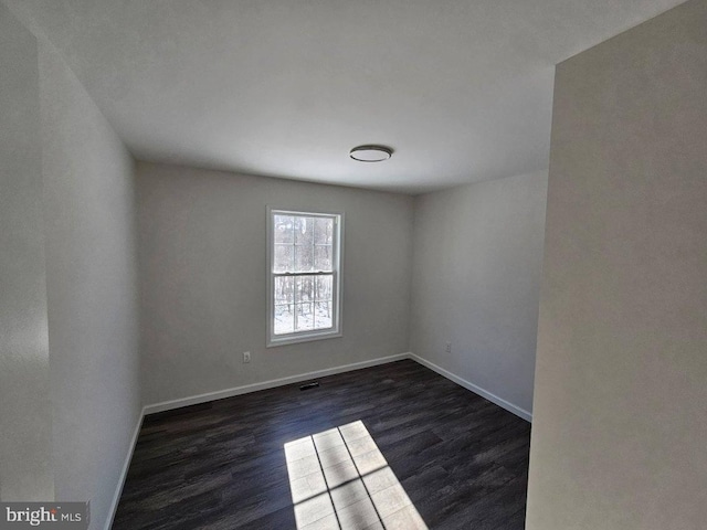 spare room featuring dark wood-type flooring and baseboards