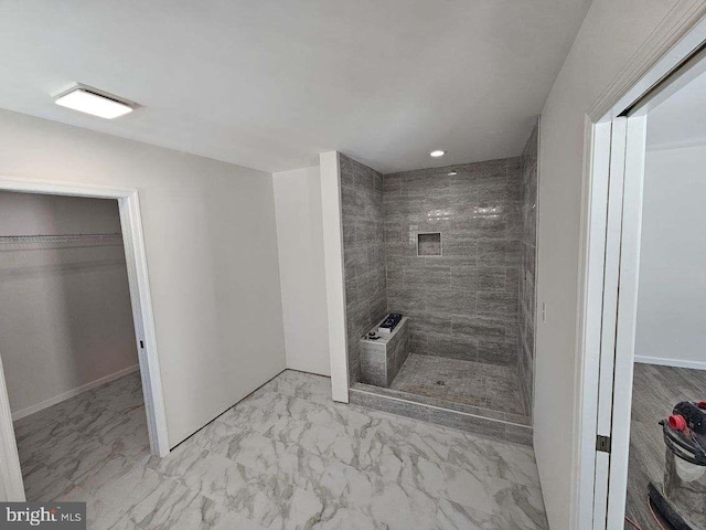 full bath featuring a tile shower, marble finish floor, a walk in closet, and baseboards