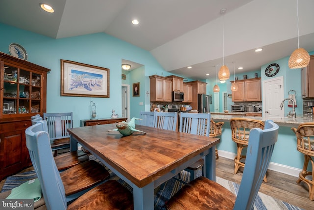 dining area with light wood-type flooring, lofted ceiling, and sink