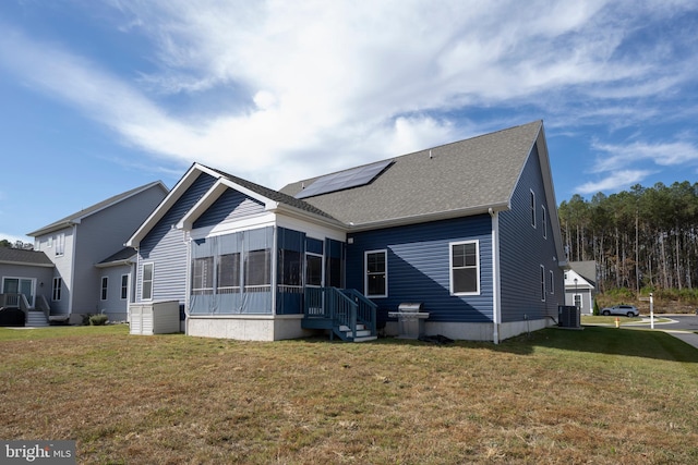 rear view of house with a sunroom, solar panels, a yard, and central AC